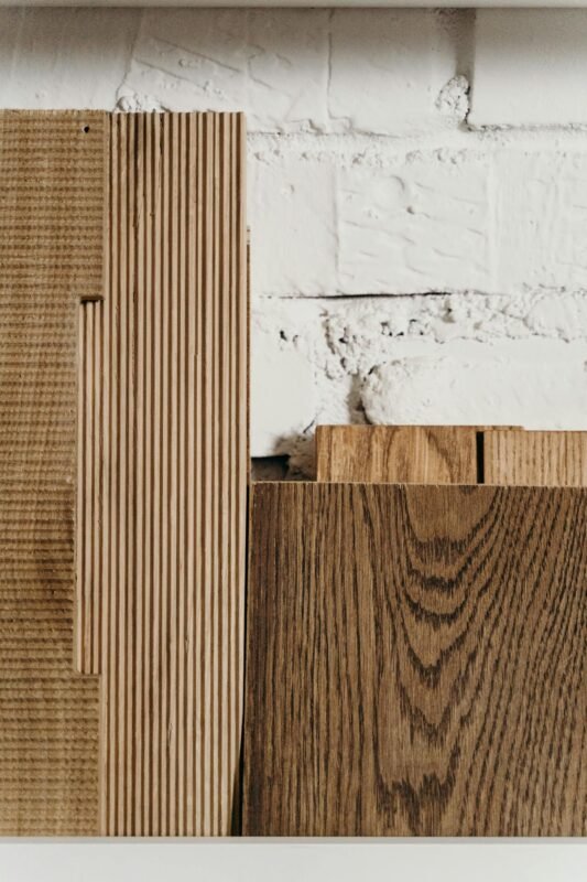 Stacked wooden planks with diverse textures leaning against a white brick wall, showcasing materials.